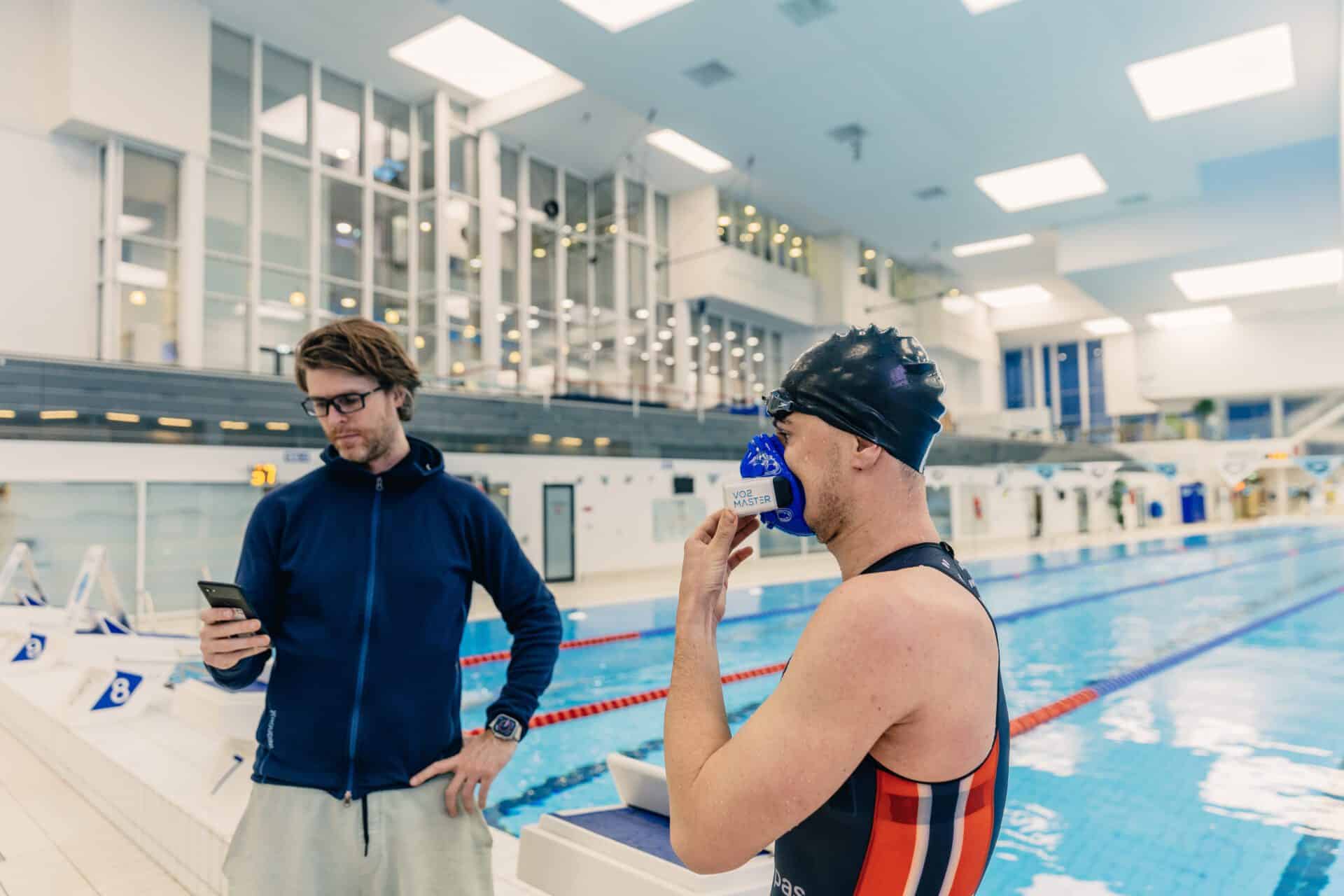 A swimming athlete from the norwegian olympic team is seen utilizing the vo2 master analyzer between training sessions to track training zones, vt1, vt2 and vo2 max. They are poolside showcasing the portability of the device.