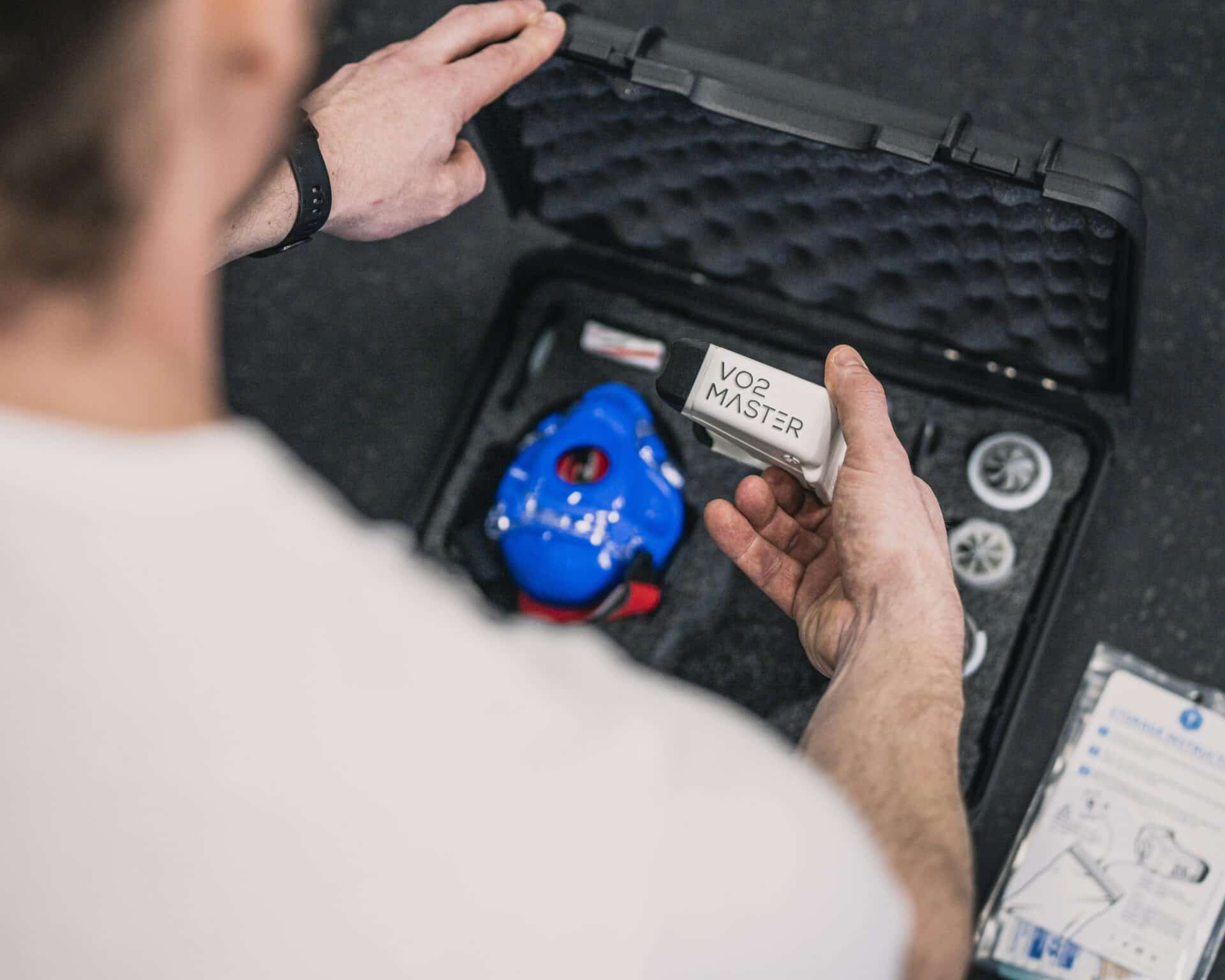 A coach is seen unboxing the vo2 master analyzer from the kit preparing to use it i a training session to track vt1 vt2 and vo2 max.  potentially for the purpose of research in the case of this image.