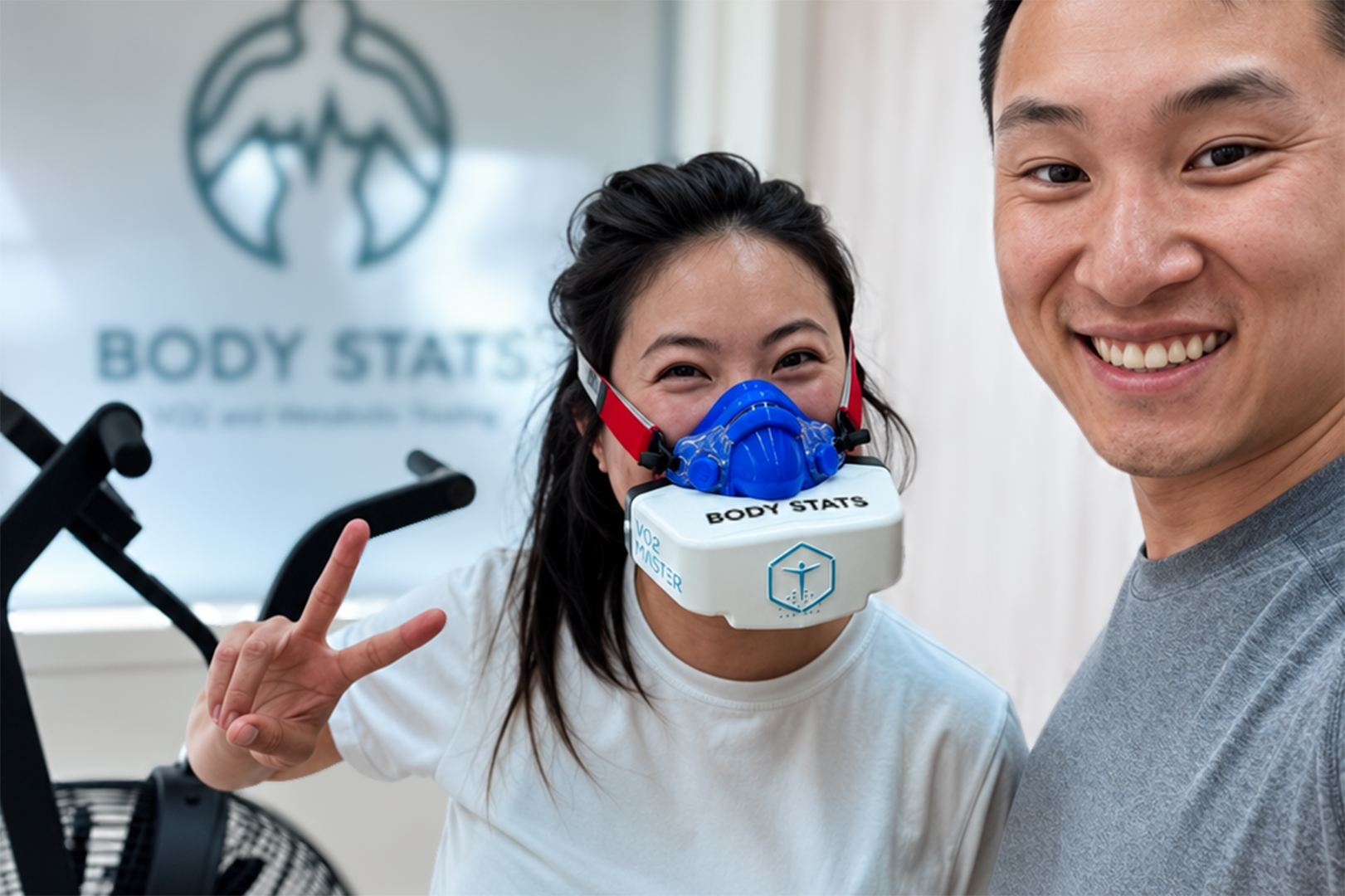 Female athlete wearing a VO2 Master metabolic testing mask at BodyStats with owner, Eric Lam, smiling beside them.