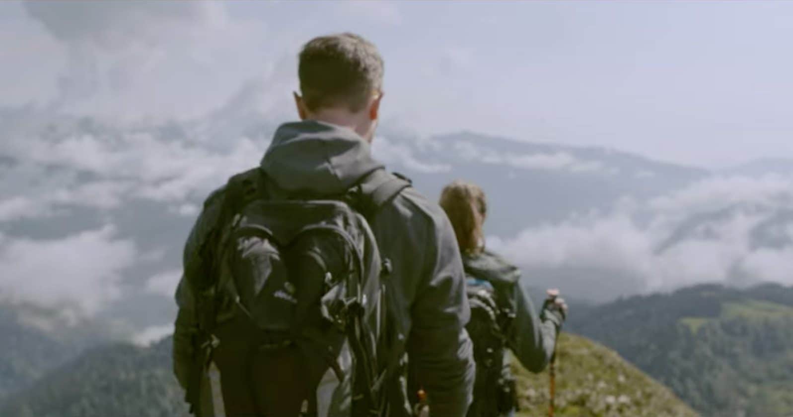 Stock photo of hikers backpacking at the top of a mountain. There is a man and a woman walking inline.