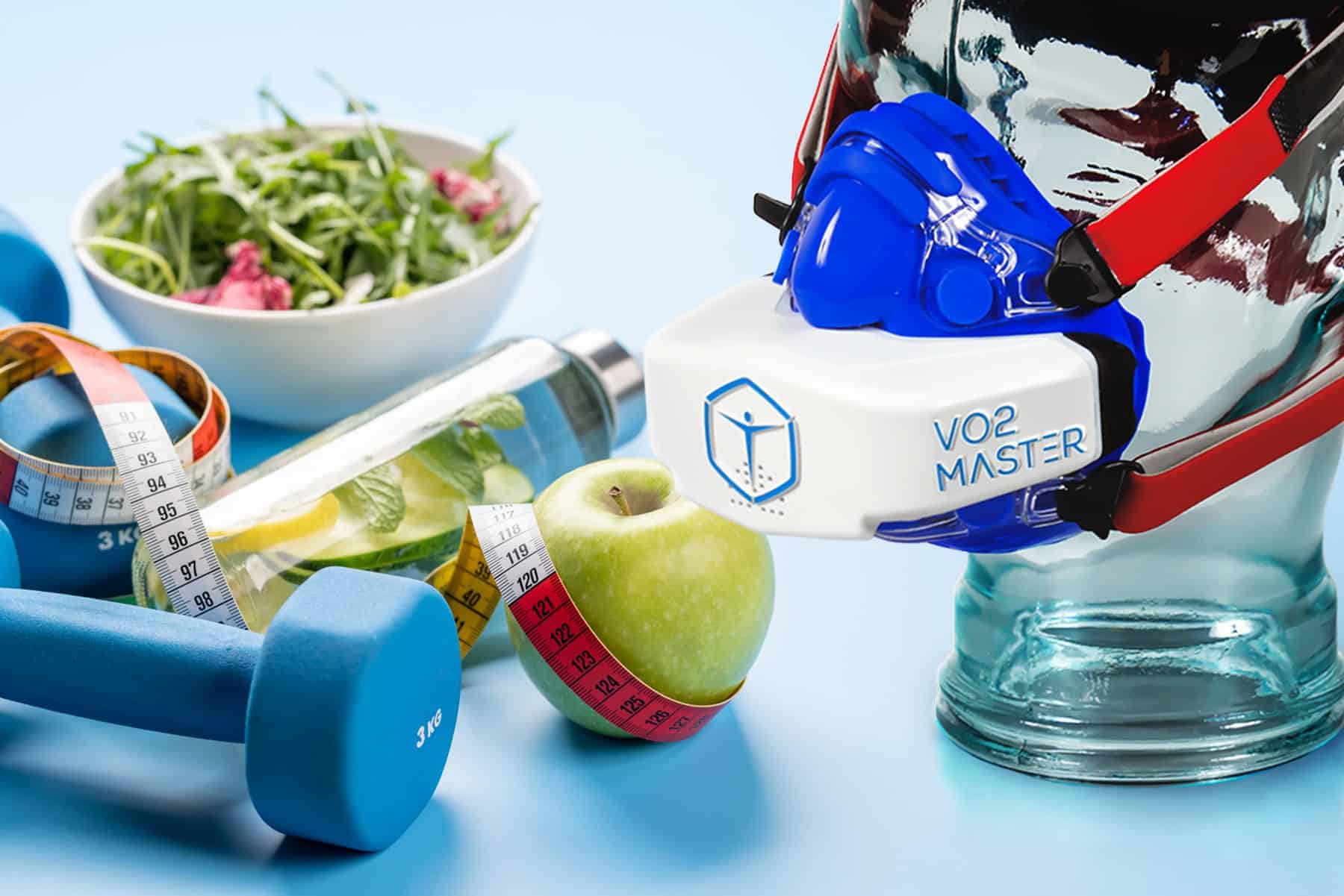 Image of VO2 Master on a display model with 3kg barbel weights, an apple, salad, water bottle with infused mint and lemon, and a measuring tape.