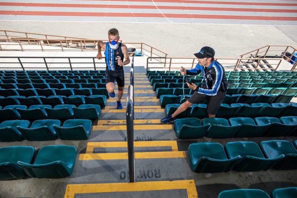 Runner sprinting up stairs with analyzer mask while trainer records with mobile phone