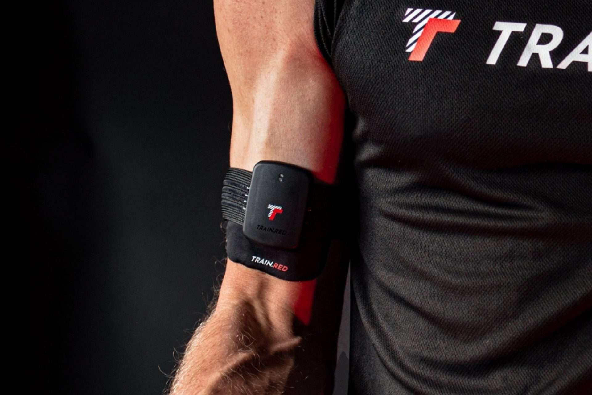 an athlete in a black tank top using a train.red monitor on his bicep