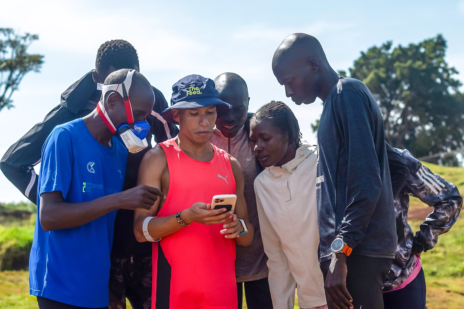 Group of athletes reviewing outdoor metabolic VO2 Master testing results on a smartphone with coach Luis Orta.