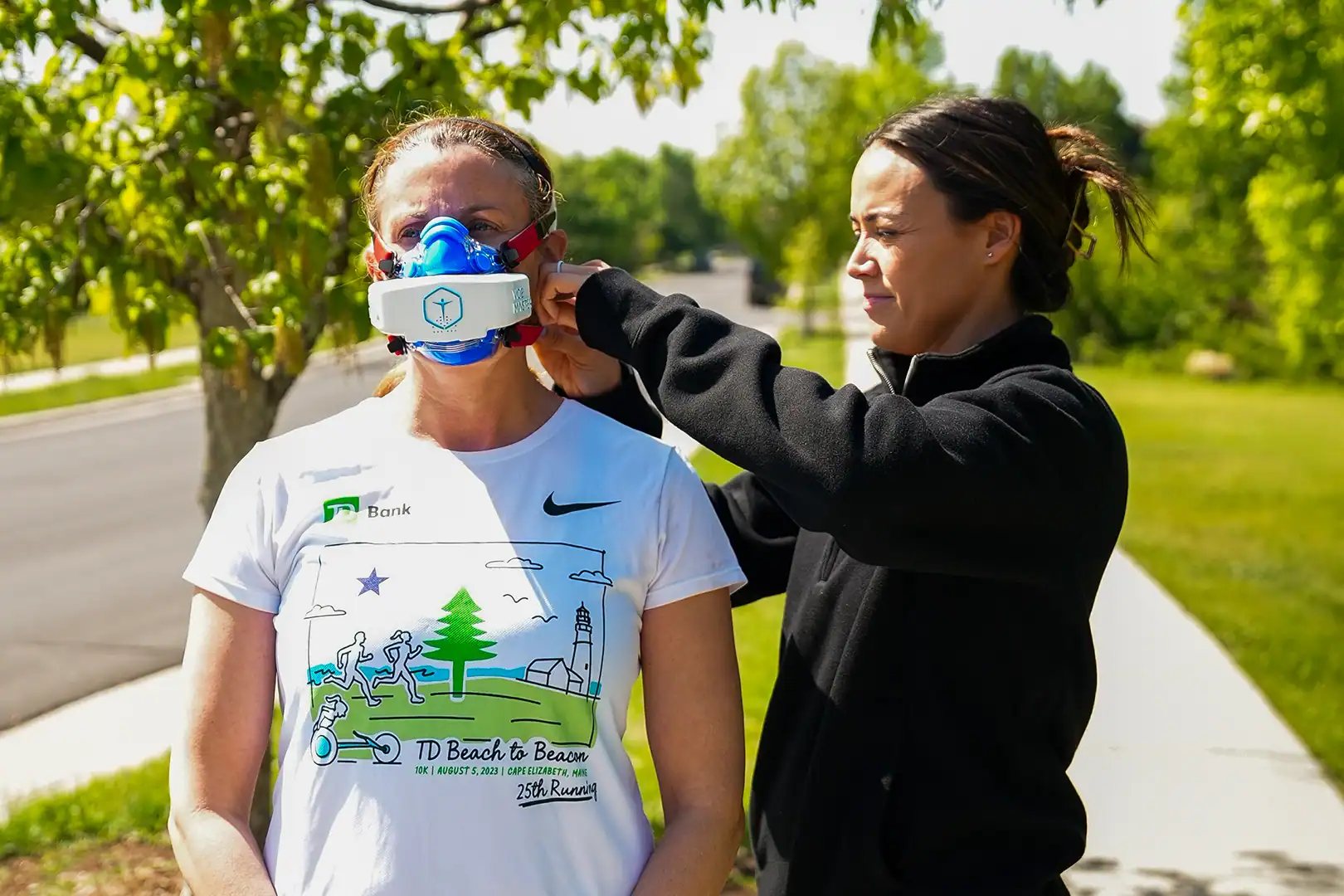 Coach Laura McDonald fitting a VO2 Master mask on an athlete during outdoor VO2 testing with portable metabolic testing equipment.