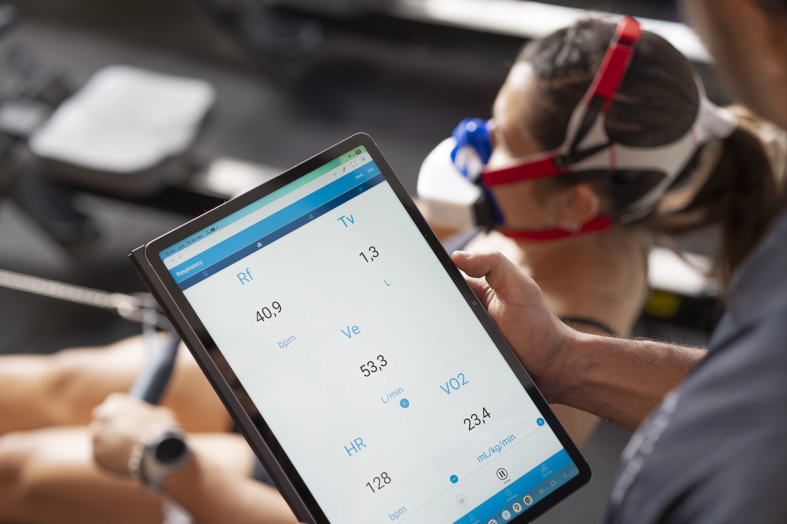 Fitness professional at Ecofiex reviewing real-time VO2 testing metrics on a tablet while a client completes a metabolic assessment with the VO2 Master analyzer.