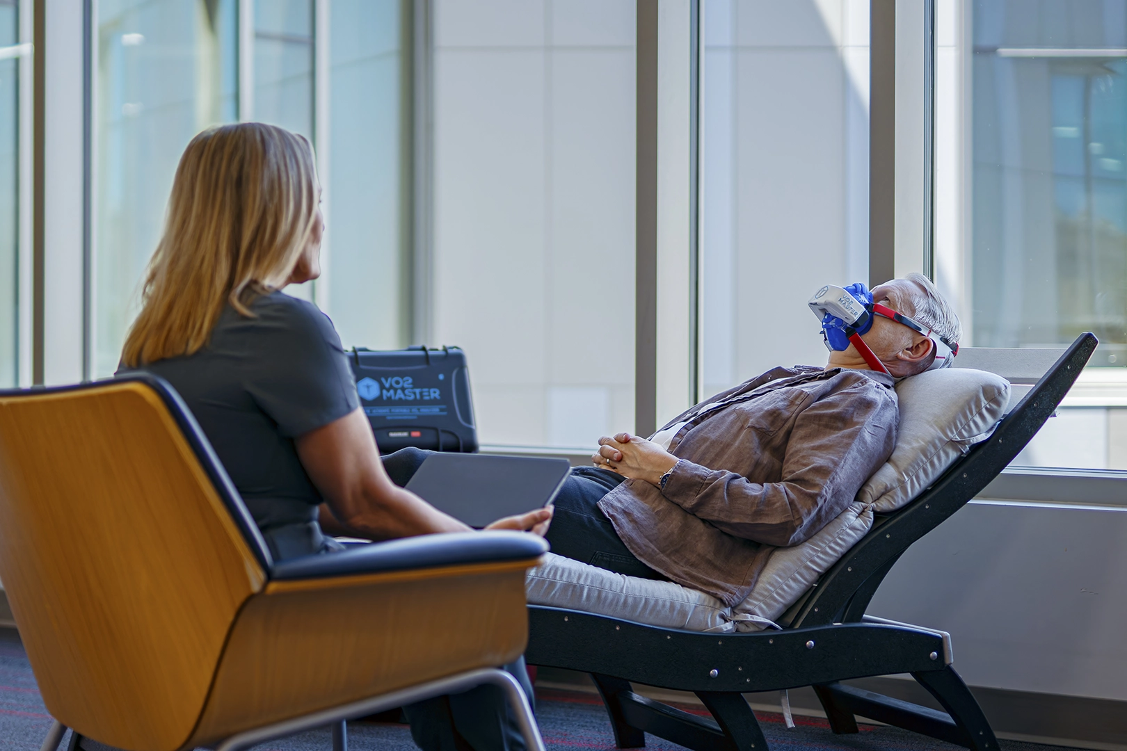 Client lying down during a resting metabolic rate test with a VO2 Master mask while a wellness professional monitors the session.