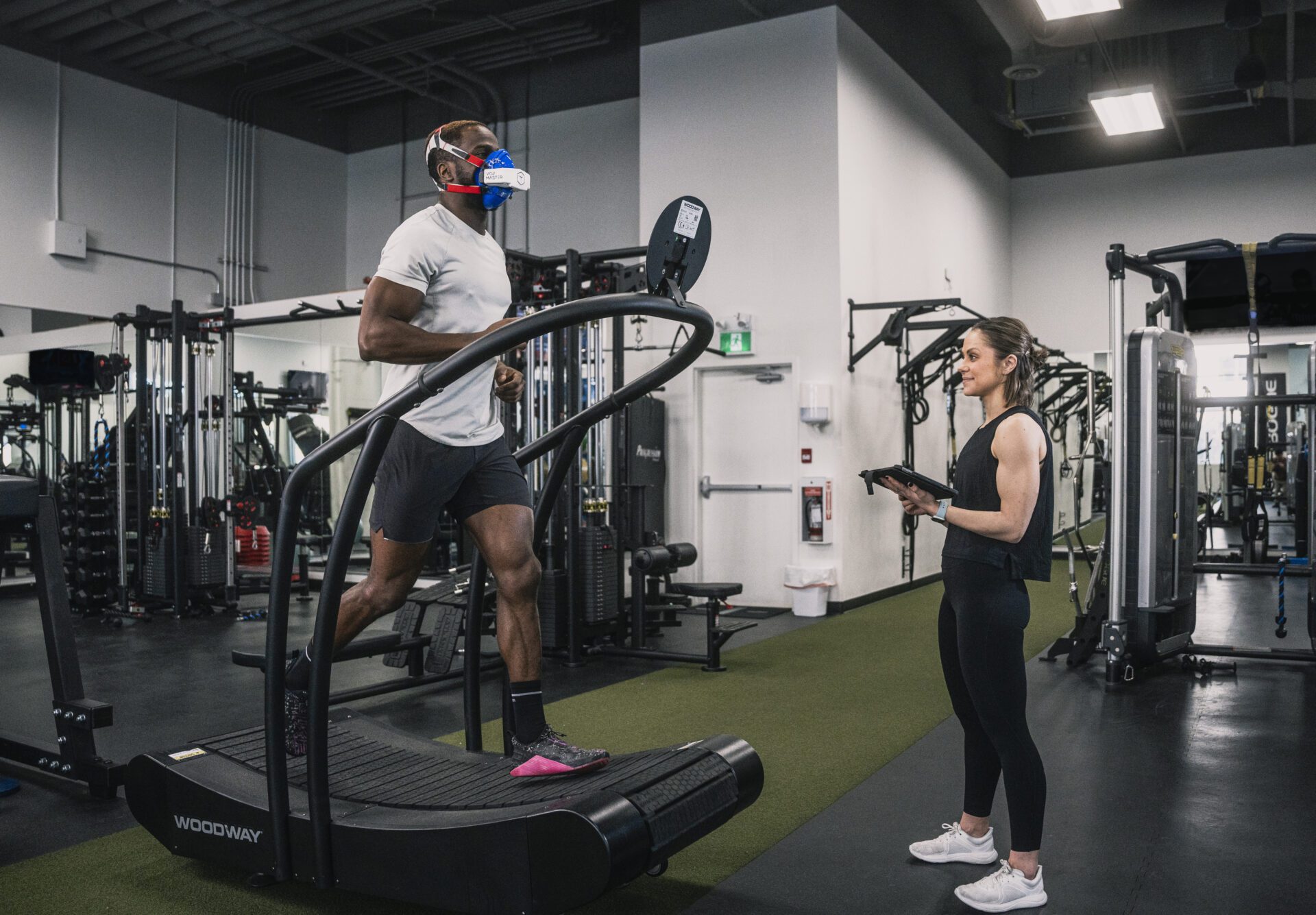 Female trainer recording performance data while a man runs on a treadmill with the VO2 Master analyzer and mask